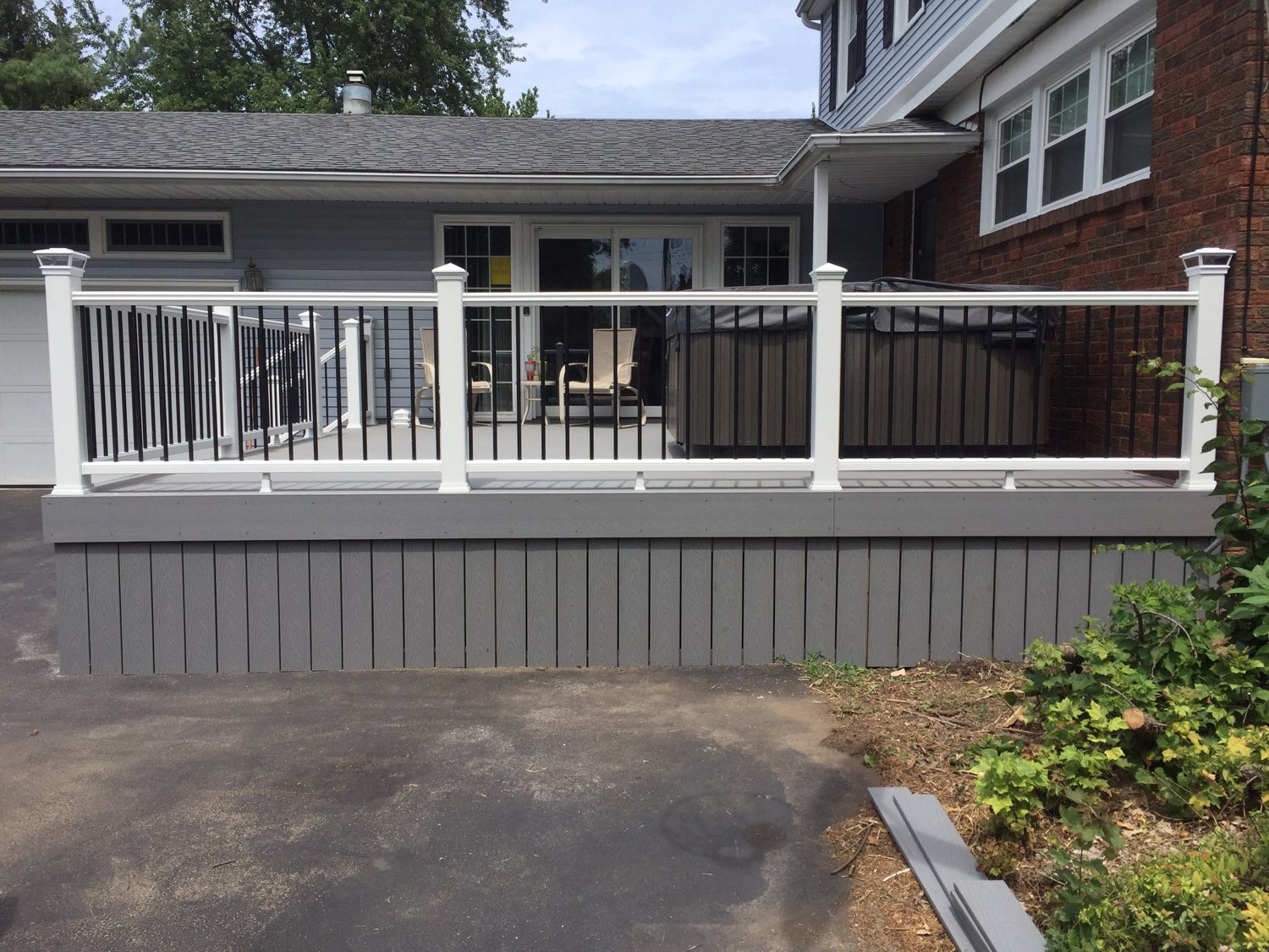 Rebuilt deck seen from the driveway, grey boards behind a white and black rail with grey skirting closing in below