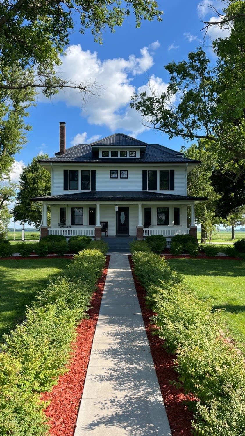 Restored white American Foursquare farmhouse in Alexis, Illinois with new siding, dark hipped roof, and a full front porch