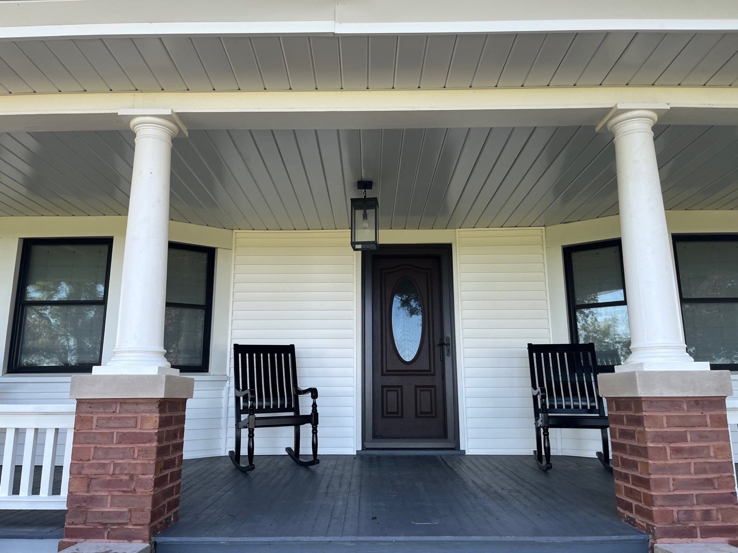 Restored farmhouse porch with white columns, a beadboard ceiling, and wooden rocking chairs by the front door