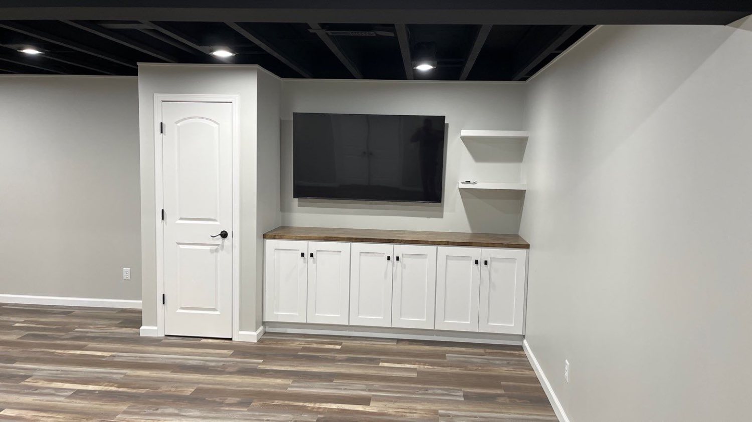 Finished basement family room with built-in white cabinetry, a mounted television, and plank flooring