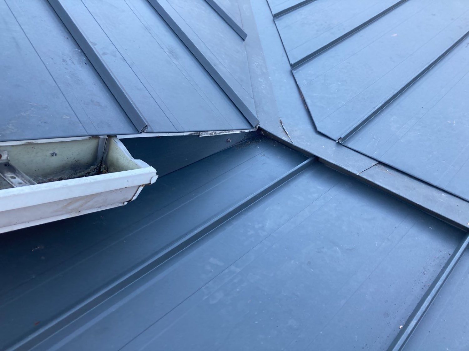 Close view of a standing-seam valley and eave detail where two roof planes meet above a gutter
