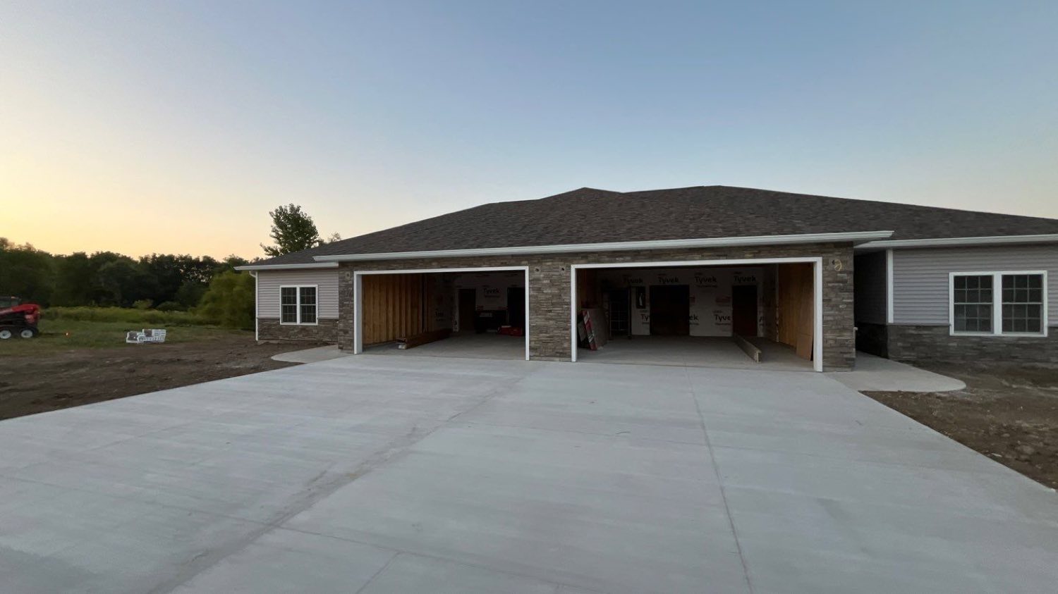 Completed villa units at dusk with stone wainscot, lap siding, and open garage bays off a poured concrete drive